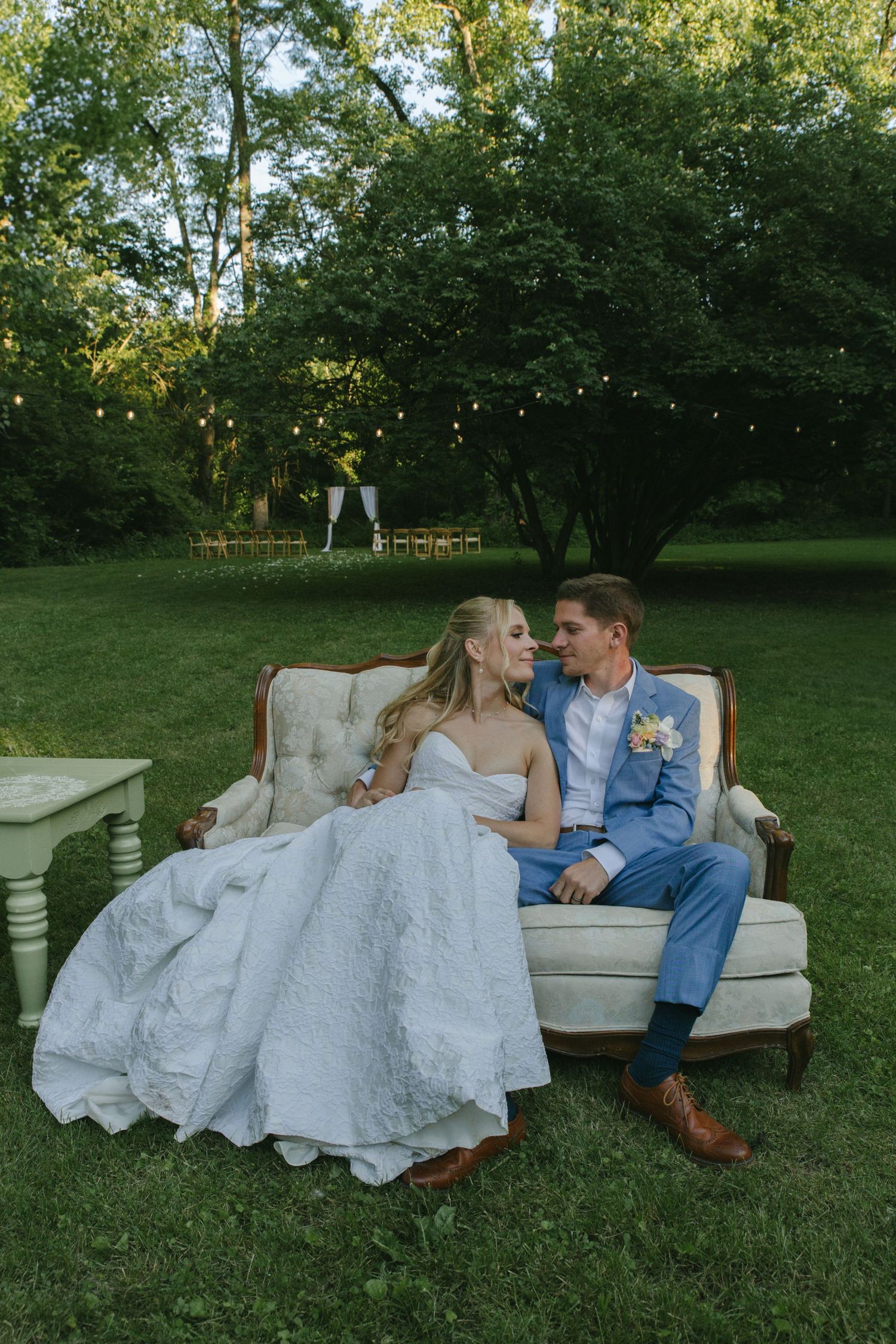 Couple lounges on a vintage sofa in a garden setting surrounded by lush greenery.