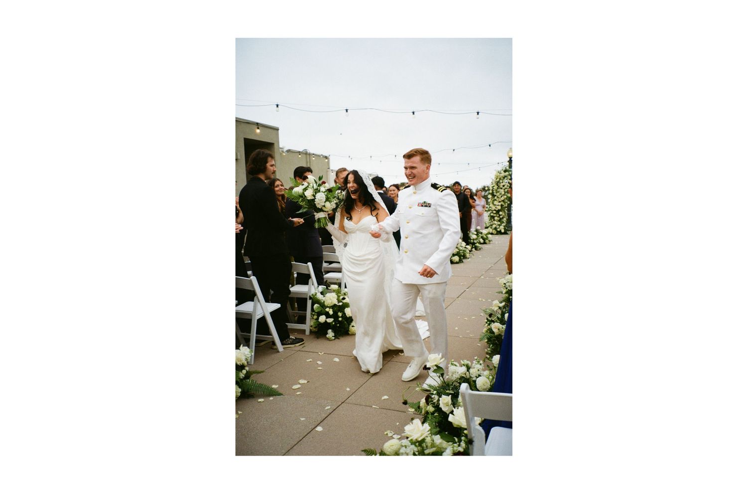 Wedding couple poses on manicured lawn with blooming flowers and trees in garden setting. Santa Barbara photographer.