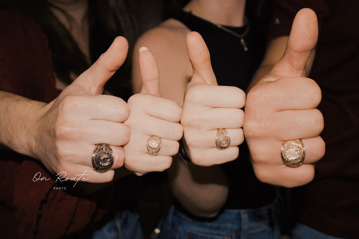 Four hands giving thumbs up gestures while wearing matching college class rings.