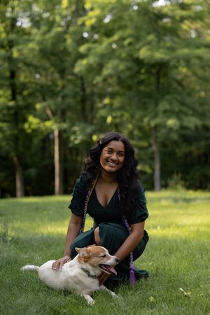 A joyful woman in a green dress sits in a grassy park while petting a white dog laying beside her.