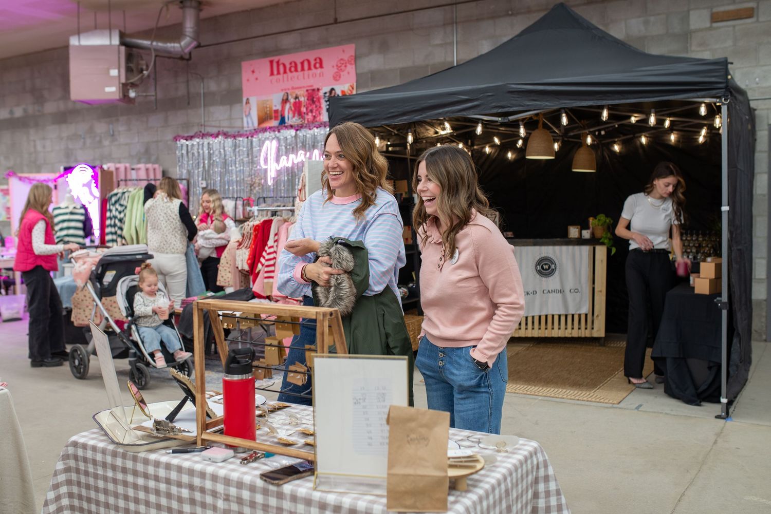 Two women browsing vendor booths at an indoor small business market event.