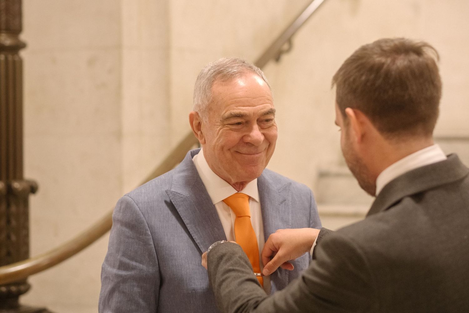Two business professionals in suits having an animated conversation in an office building hallway.