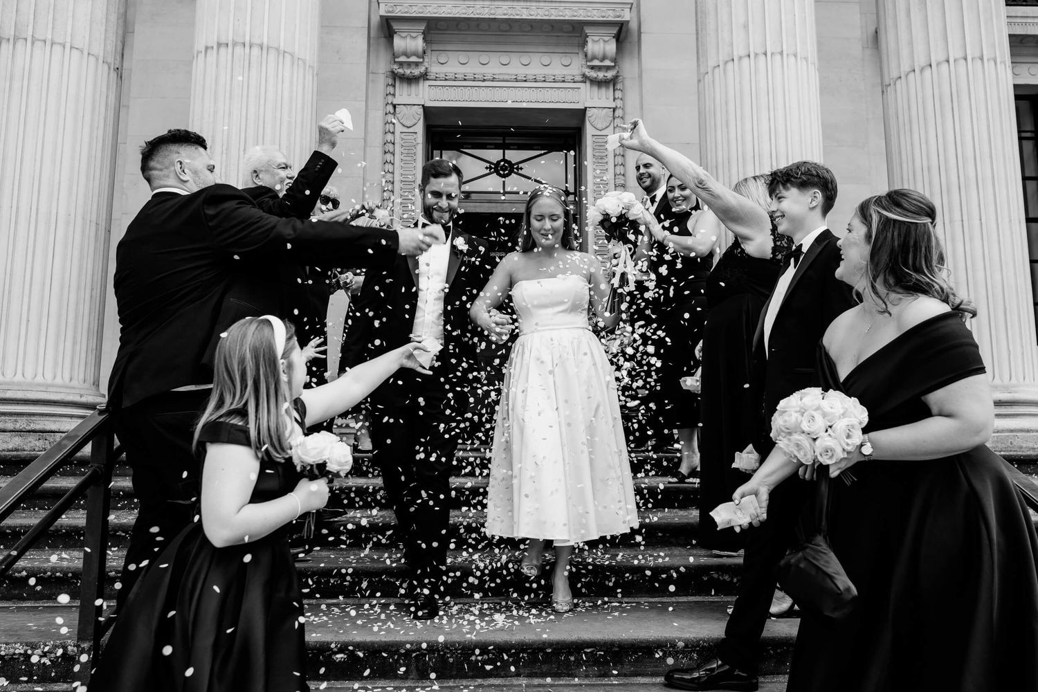 A collection of candid black and white wedding photos showing joyful moments between guests and participants at outdoor venues.