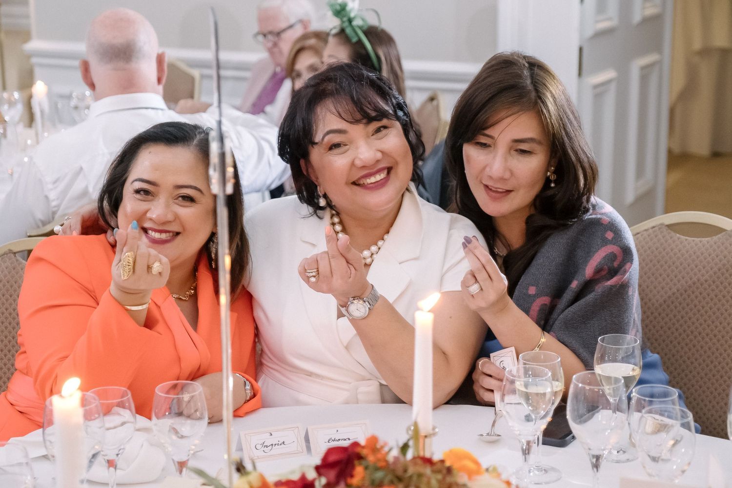 Three guests enjoying a celebratory dinner event with candles and wine glasses at an elegant table setting.