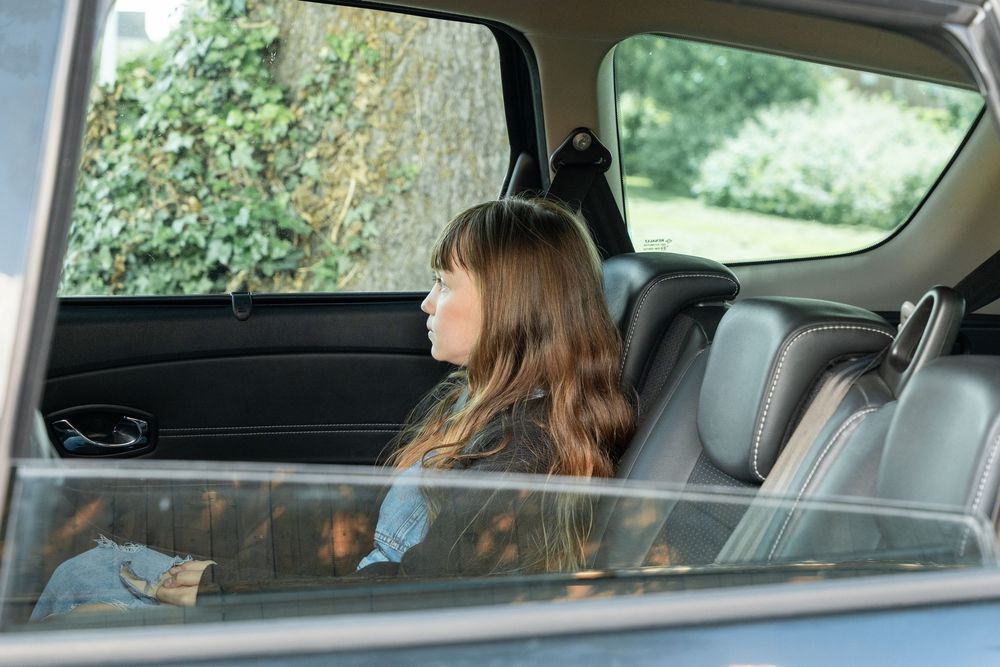A passenger sits in the backseat of a car looking out the window while holding a mobile device.