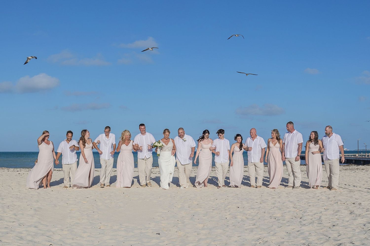 Bride and groom walk along the beach with friends, creating lasting memories of their wedding day.