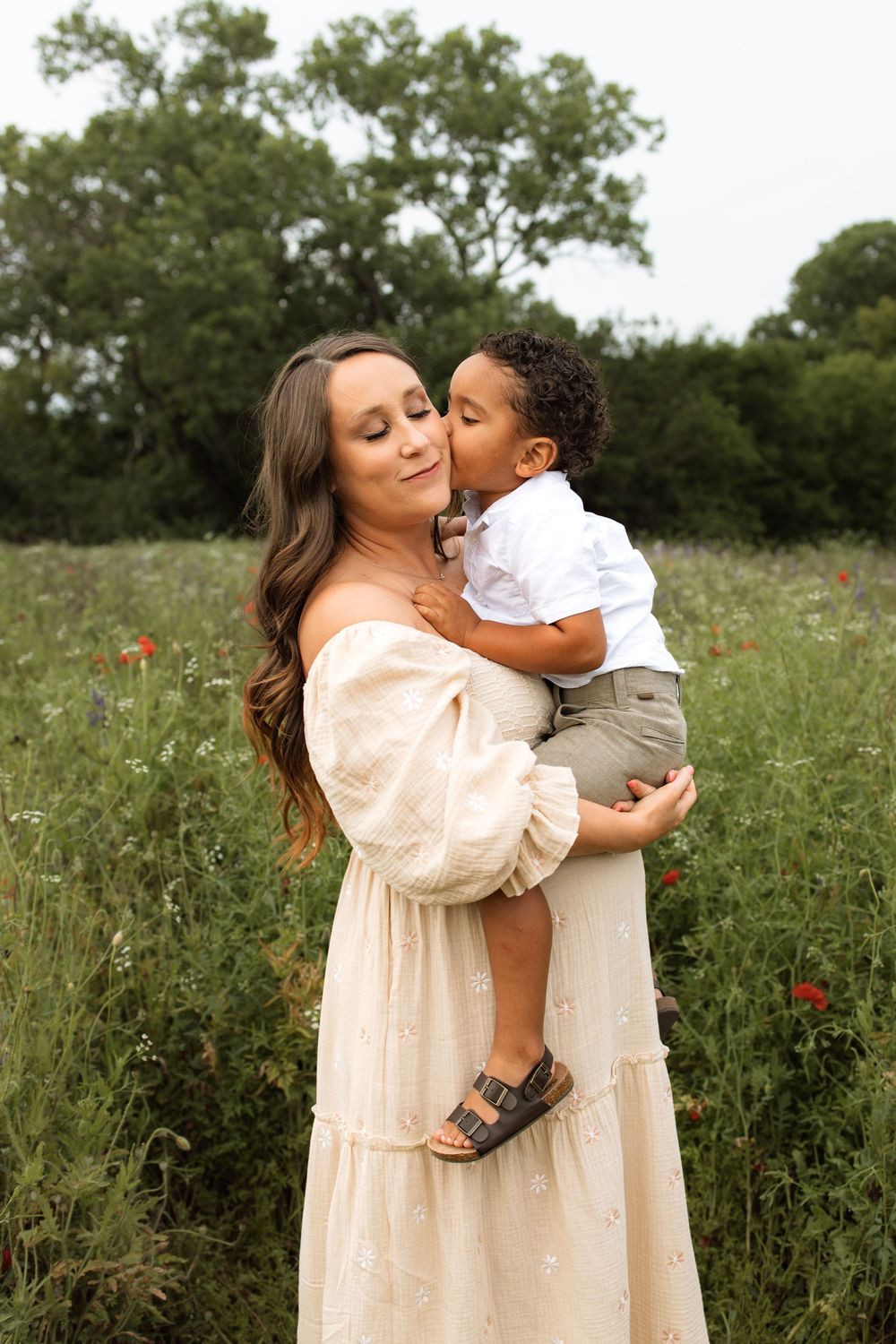 A tender moment captured outdoors in a wildflower field with a cream-colored dress against a natural green backdrop.