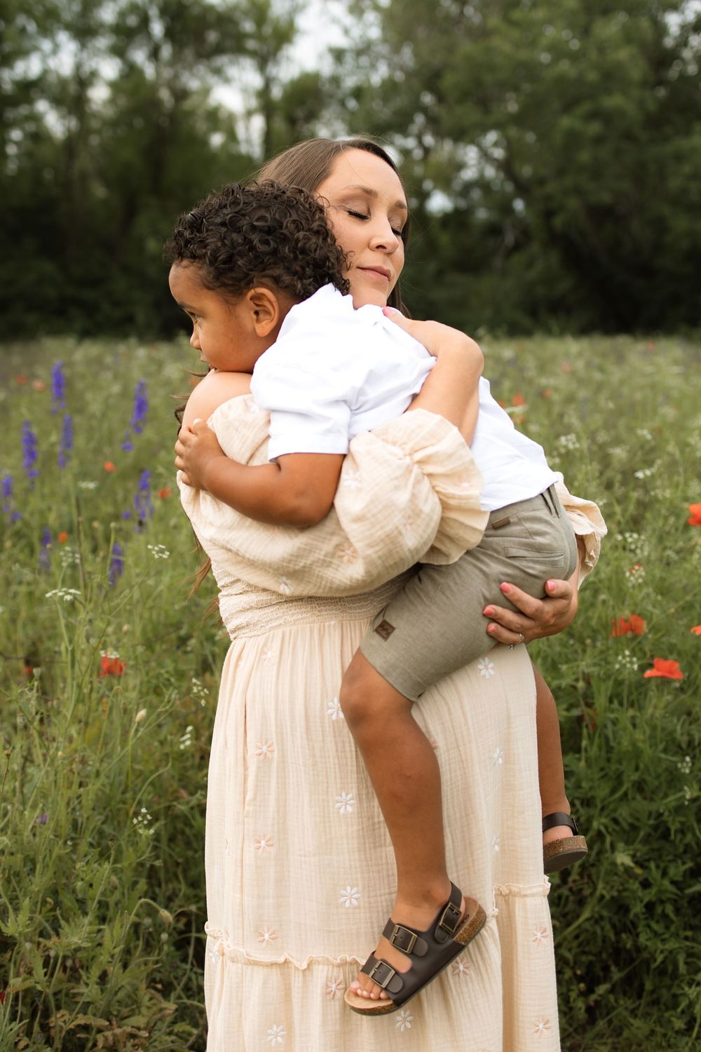 A tender moment captured in a wildflower meadow with white dress and soft summer light.