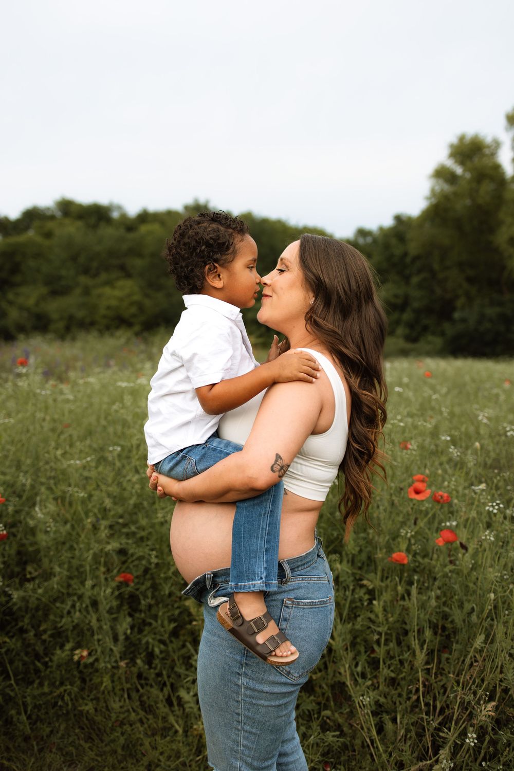 A pregnant woman and child embrace in a wildflower meadow with red poppies on a summer afternoon.