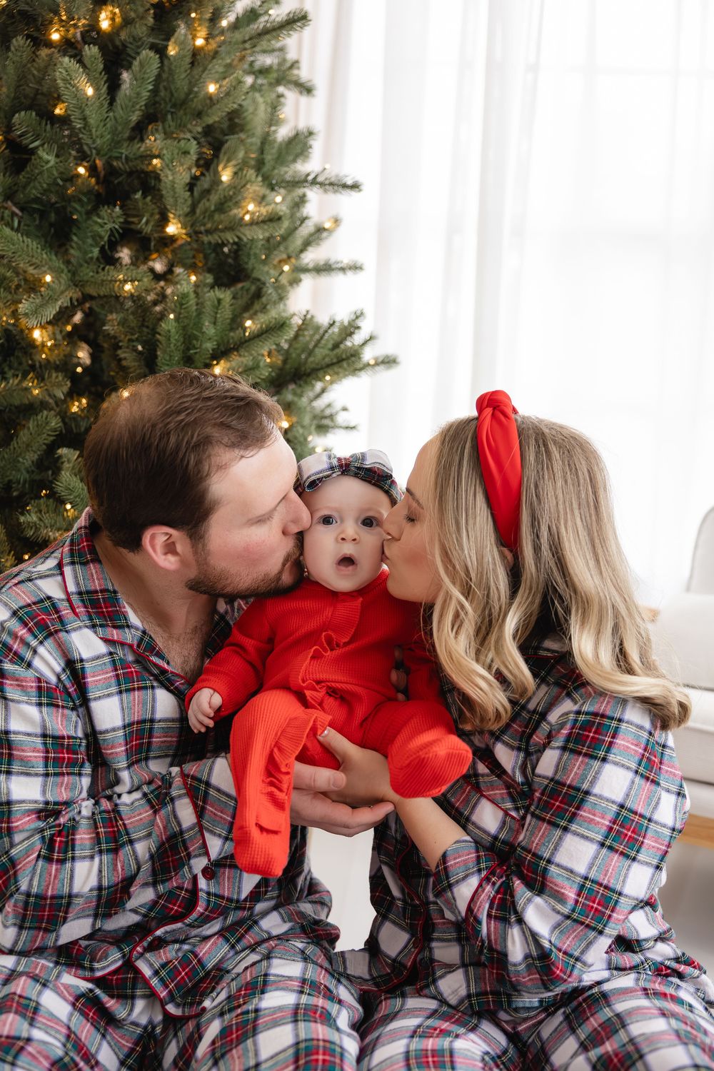 A family in matching plaid pajamas shares loving kisses by their Christmas tree in a series of candid photos.