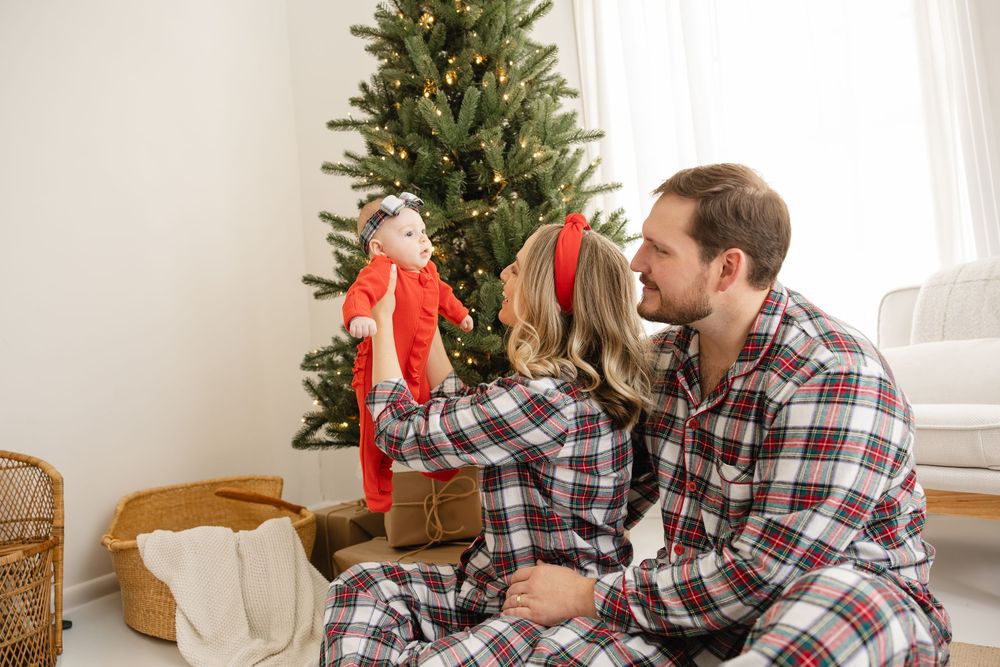 Couple in plaid shirts decorates a Christmas tree together in a bright, cozy living room.