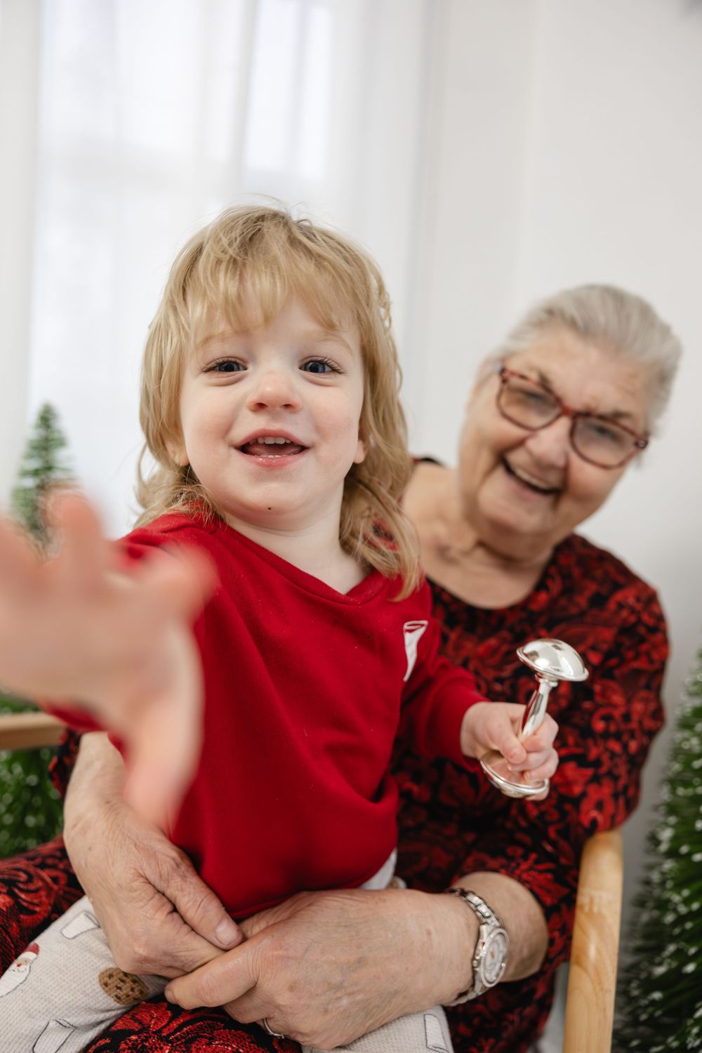 Elderly grandmother holding a smiling toddler in a red shirt during a Christmas holiday photo session.