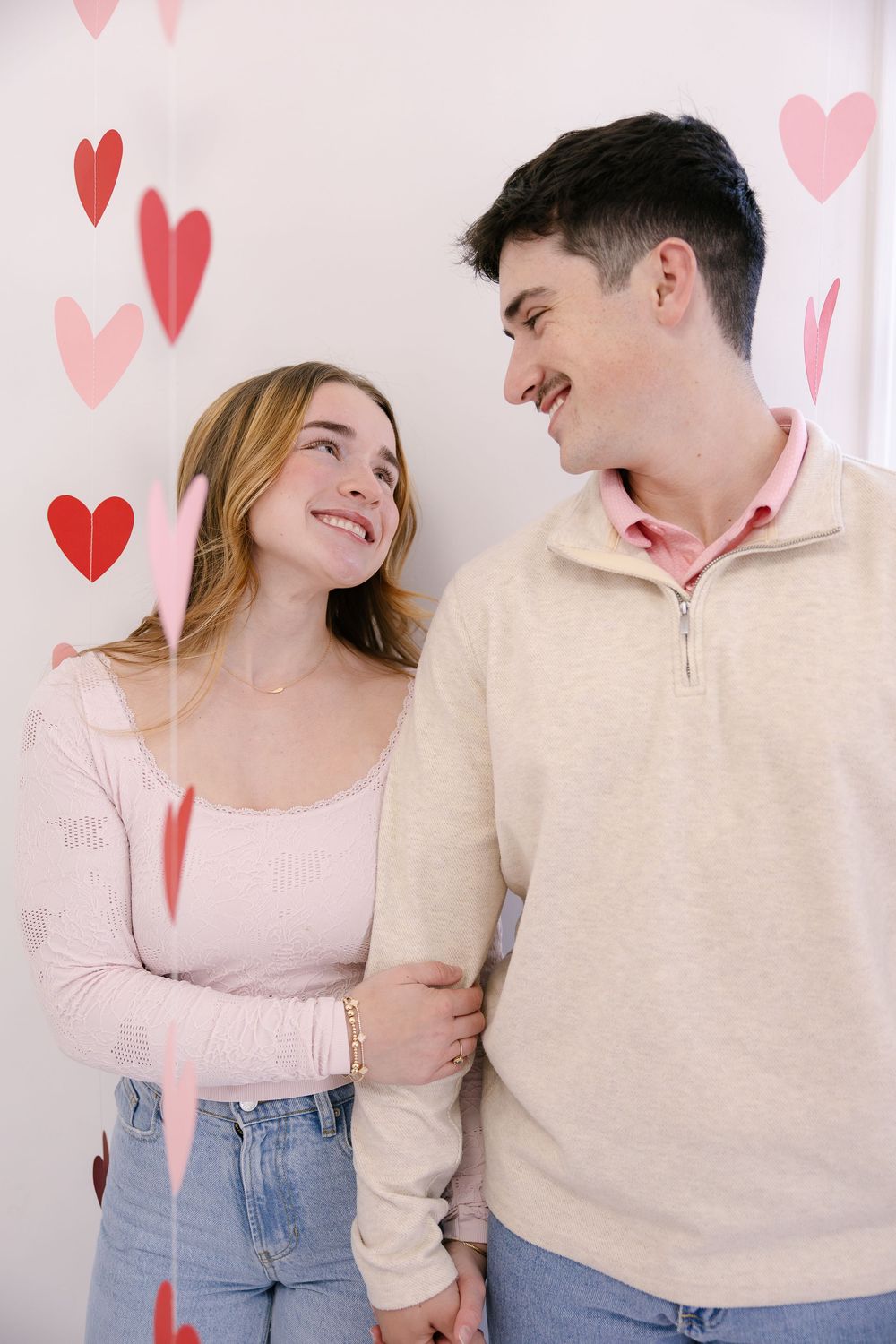 Happy couple in casual outfits sharing romantic moments against a pink background with heart decorations.