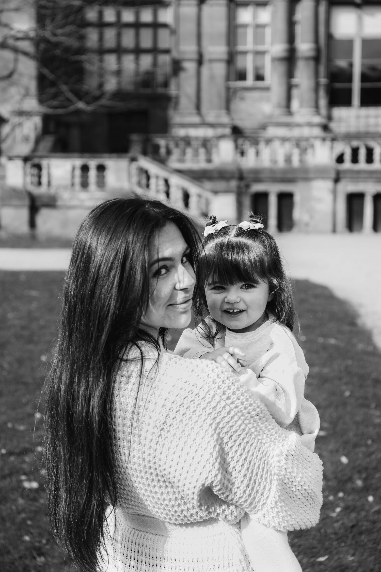 A mother and child wearing matching white sweaters embrace and laugh together on an autumn lawn during Family shoot in Nottingham