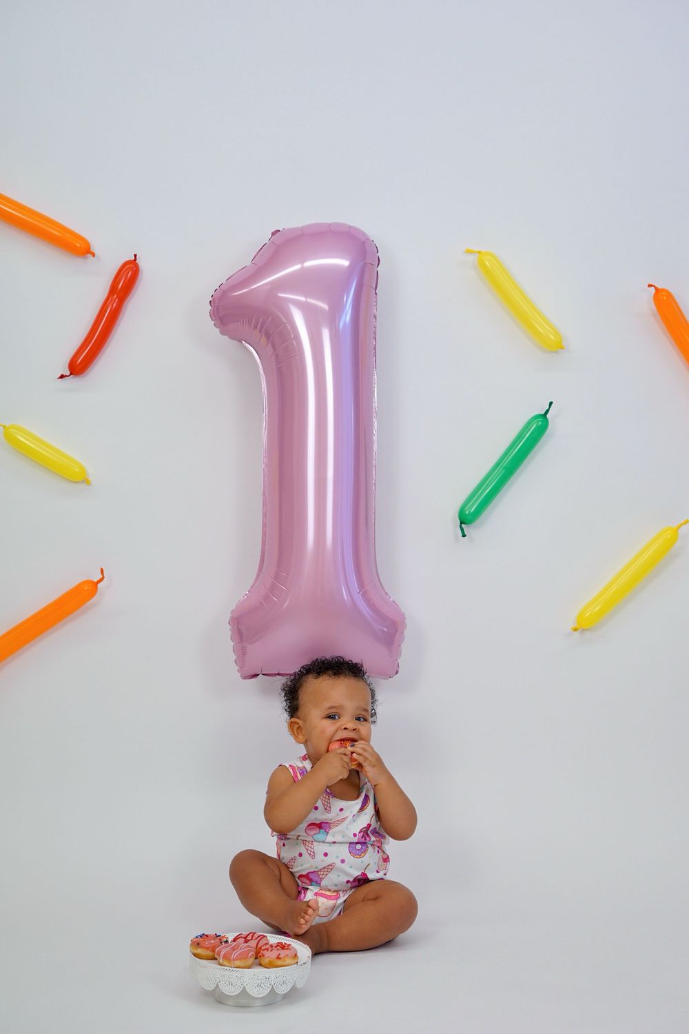 First birthday celebration setup with pink number one balloon and colorful decorative elements against white background.