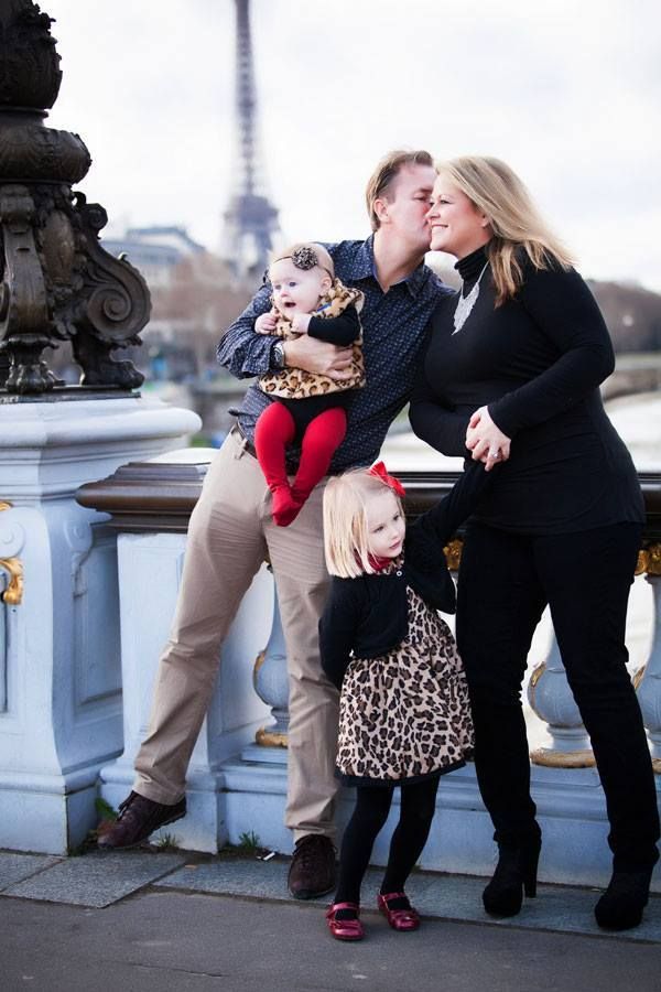 A family shares a tender moment together on a bridge in Paris with the Eiffel Tower visible in the background.