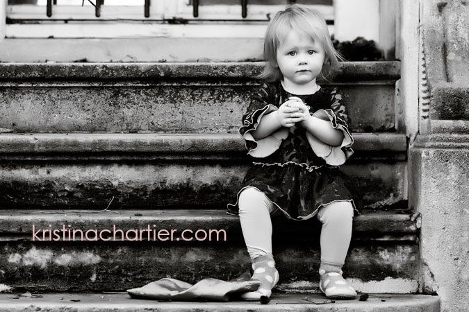 A candid black and white photograph of a small child sitting on stone steps while holding something in their hands.