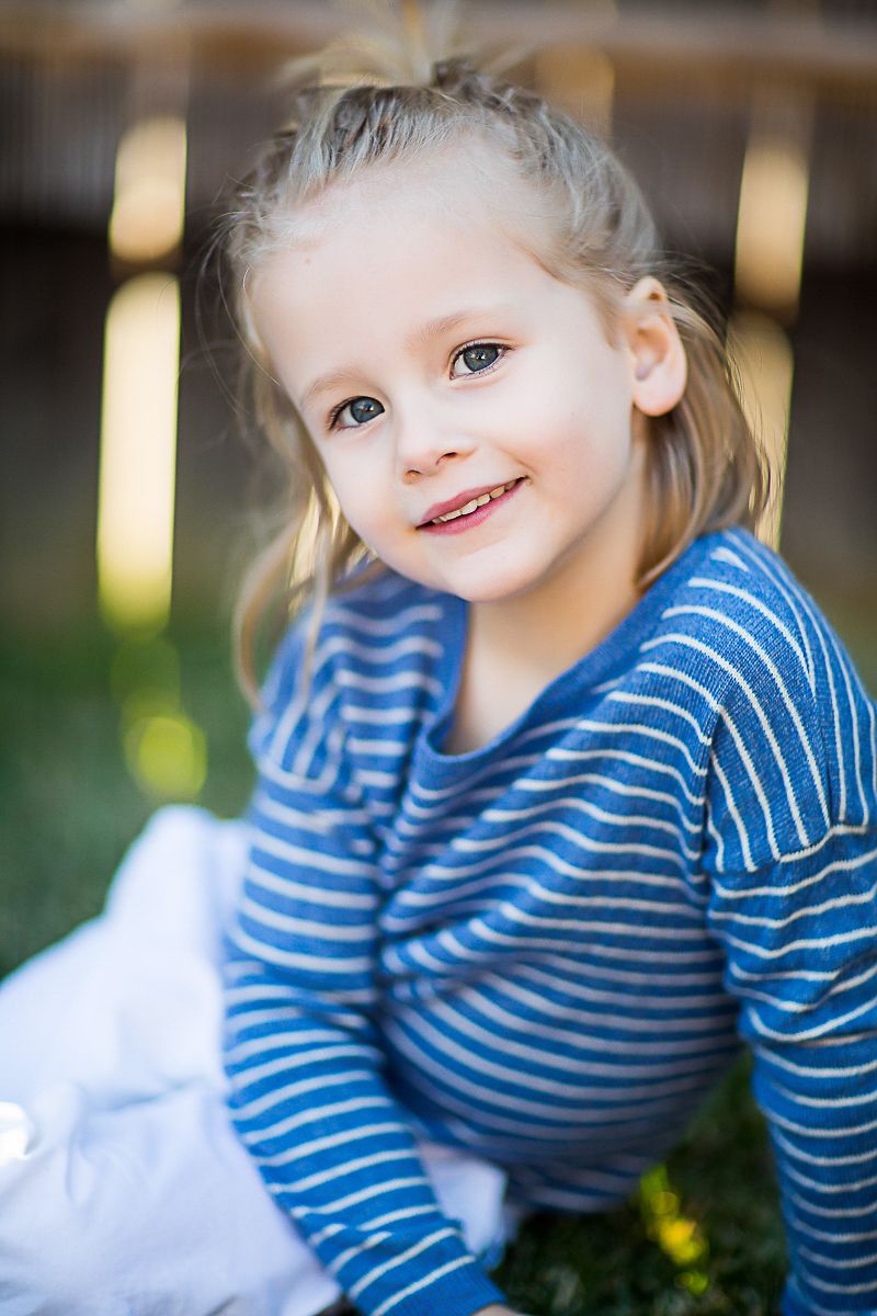 Young child in blue and white striped shirt sitting outdoors in natural lighting.
