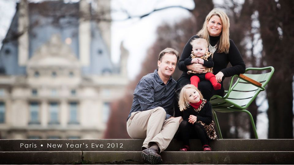 A family sits together outdoors on park benches with a blurred castle-like building in the background on New Year's Eve.