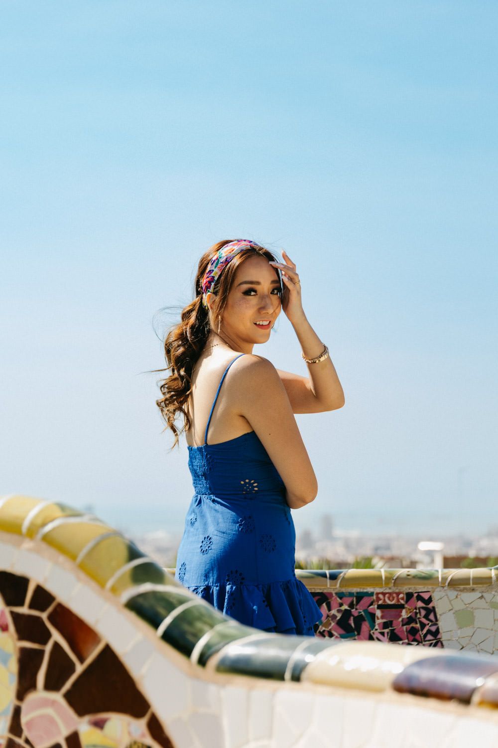 Person in blue dress poses against ornate architecture with blue sky background.