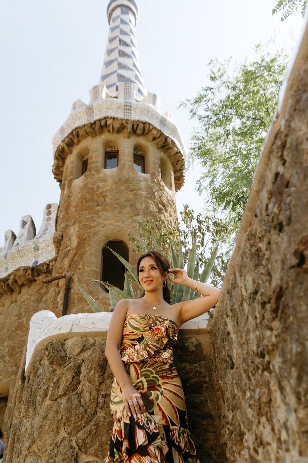 Person in floral dress poses near stone tower with architectural details.