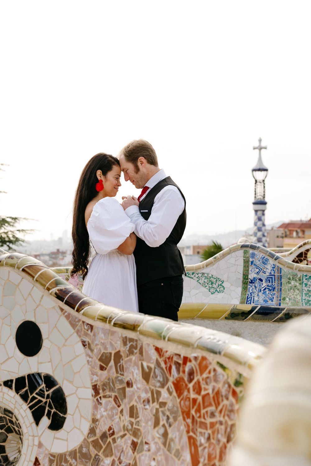 Romantic couple embraces against the colorful mosaic backdrop of Park Guell in Barcelona.