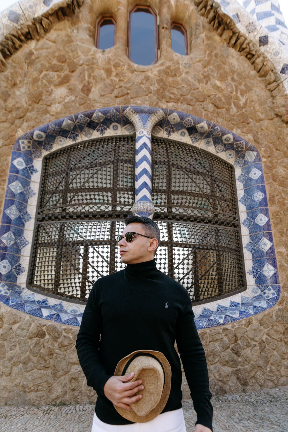 Stylish person poses with hat against ornate Moorish-style window architecture.