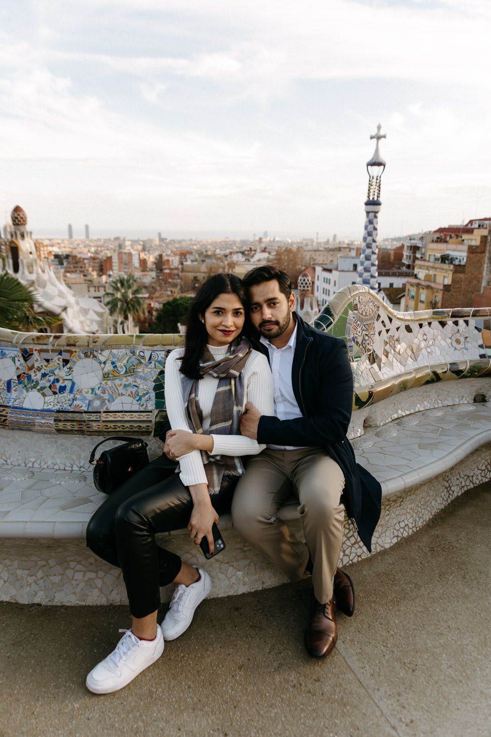 Couple relaxes on mosaic bench overlooking Barcelona's iconic skyline.