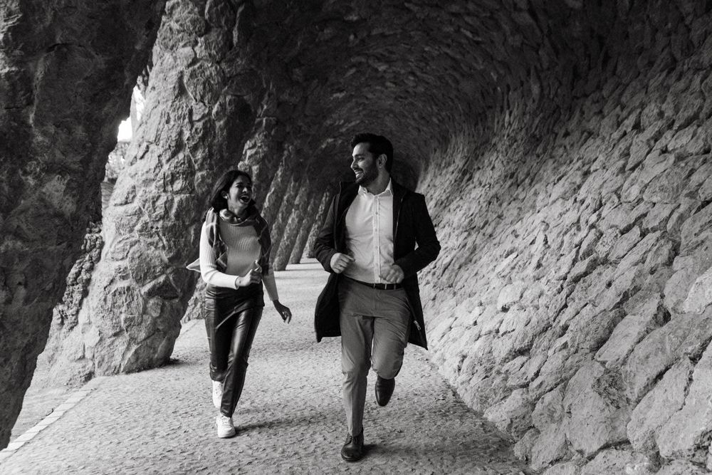 Black and white photo of couple walking through stone archway passage.