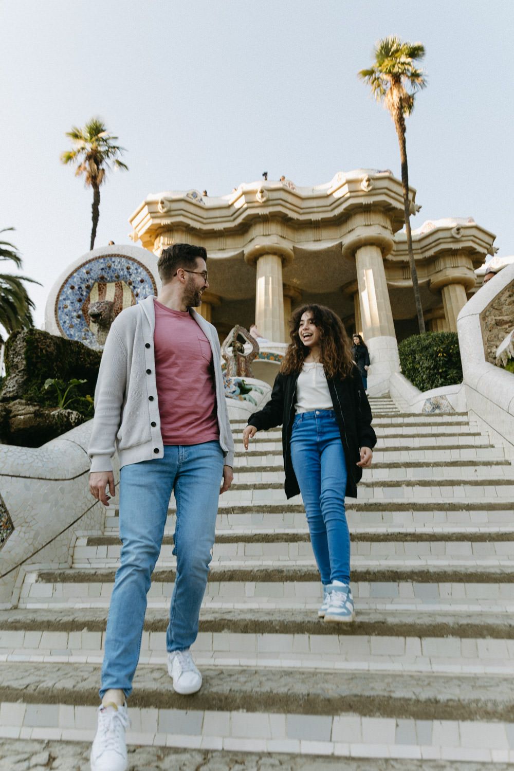 Couple walking down the grand staircase at Park Guell with palm trees in the background.
