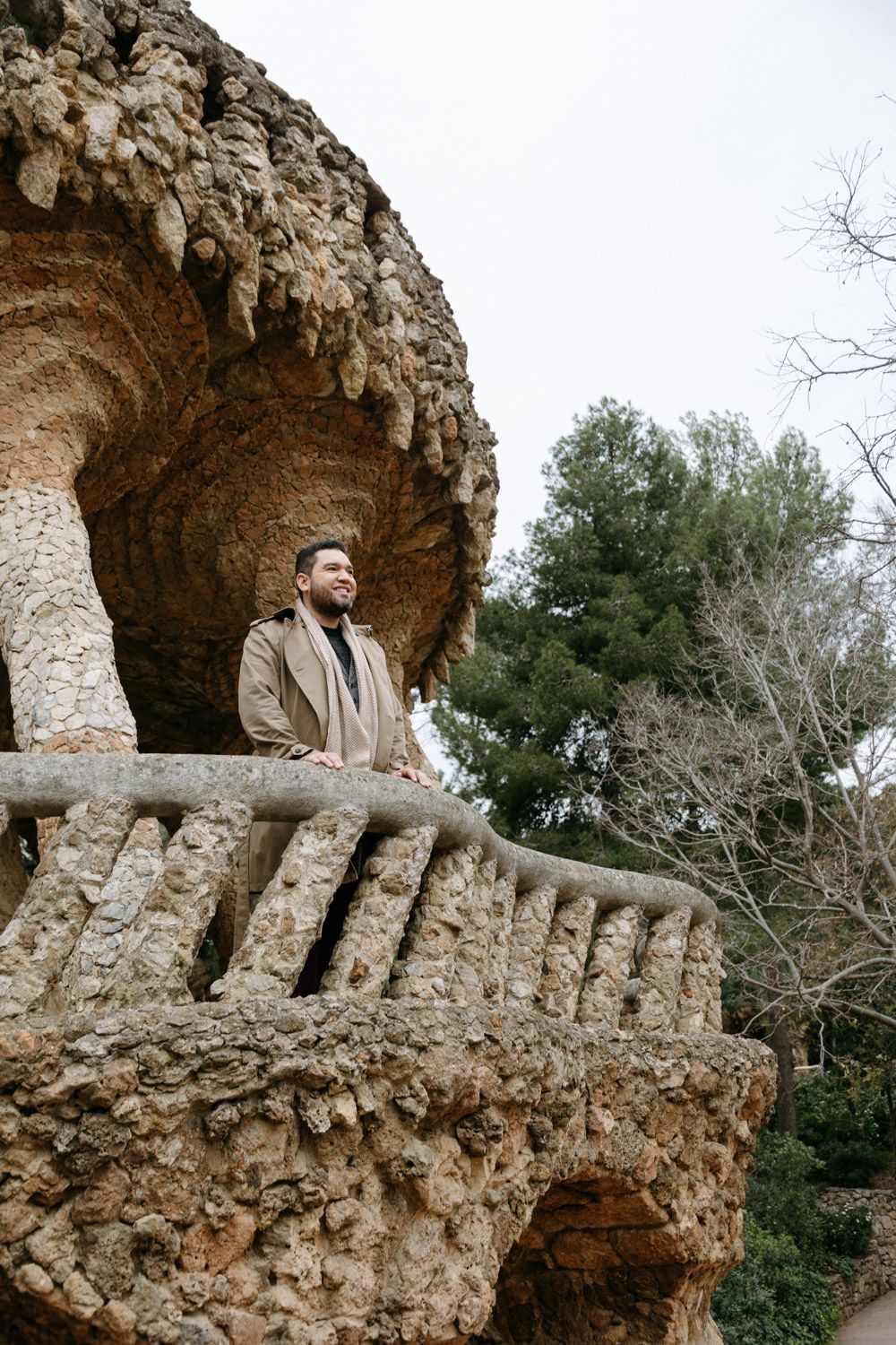 Person standing on a decorative stone balcony overlooking a park landscape.