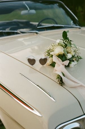 White wedding bouquet with roses and heart decorations on classic cream-colored car hood.
