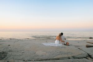 Couple sitting on rocky coastal shore during golden sunset.