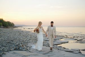 Newlyweds walking hand in hand along rocky beach at dusk.