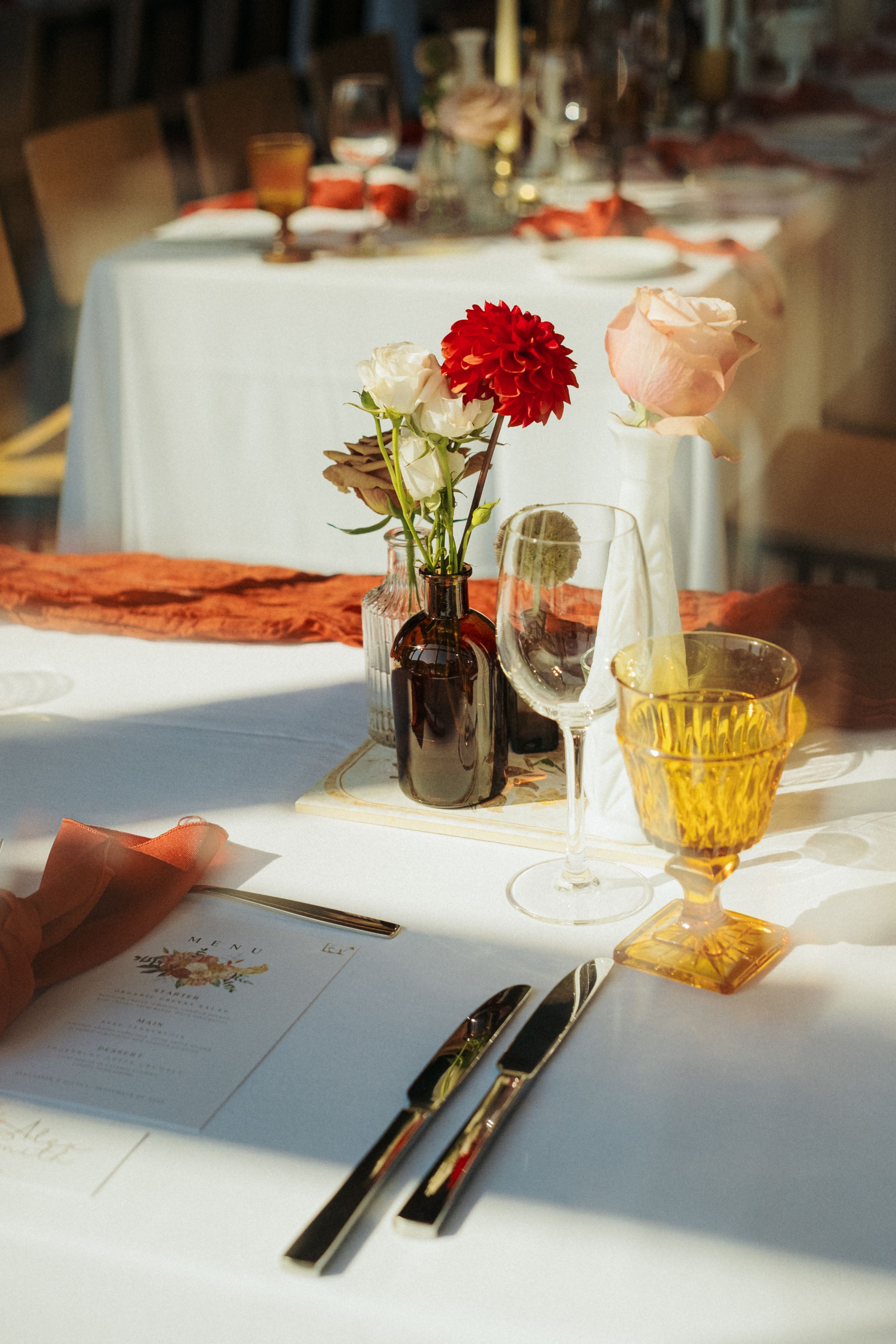 Elegant wedding reception table setting with flowers and glassware in warm sunlight.