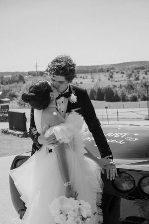 Black and white romantic wedding photo of couple embracing by vintage car.