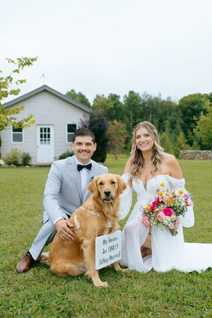 Happy couple poses on grass with their golden retriever and wedding signage.