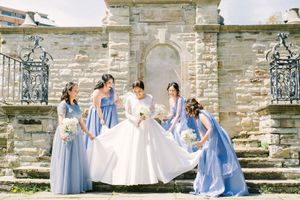 Wedding party in light blue dresses and white gown pose on stone steps.