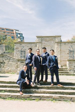 Groomsmen in navy suits pose casually on stone steps at historic venue.