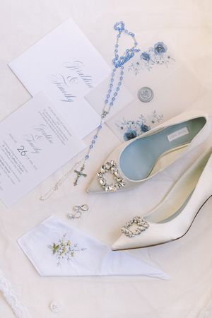 Elegant white bridal shoes and wedding stationery with delicate blue floral accents.