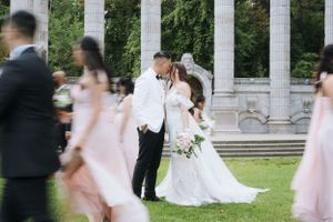 Wedding party gathered under classical white stone columns surrounded by lush greenery.