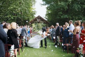 Wedding ceremony recessional with guests throwing flower petals under garden gazebo.