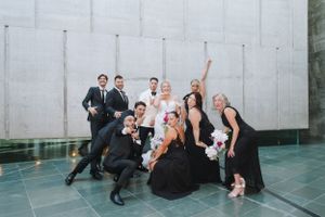 Wedding party posing playfully against modern concrete architecture.