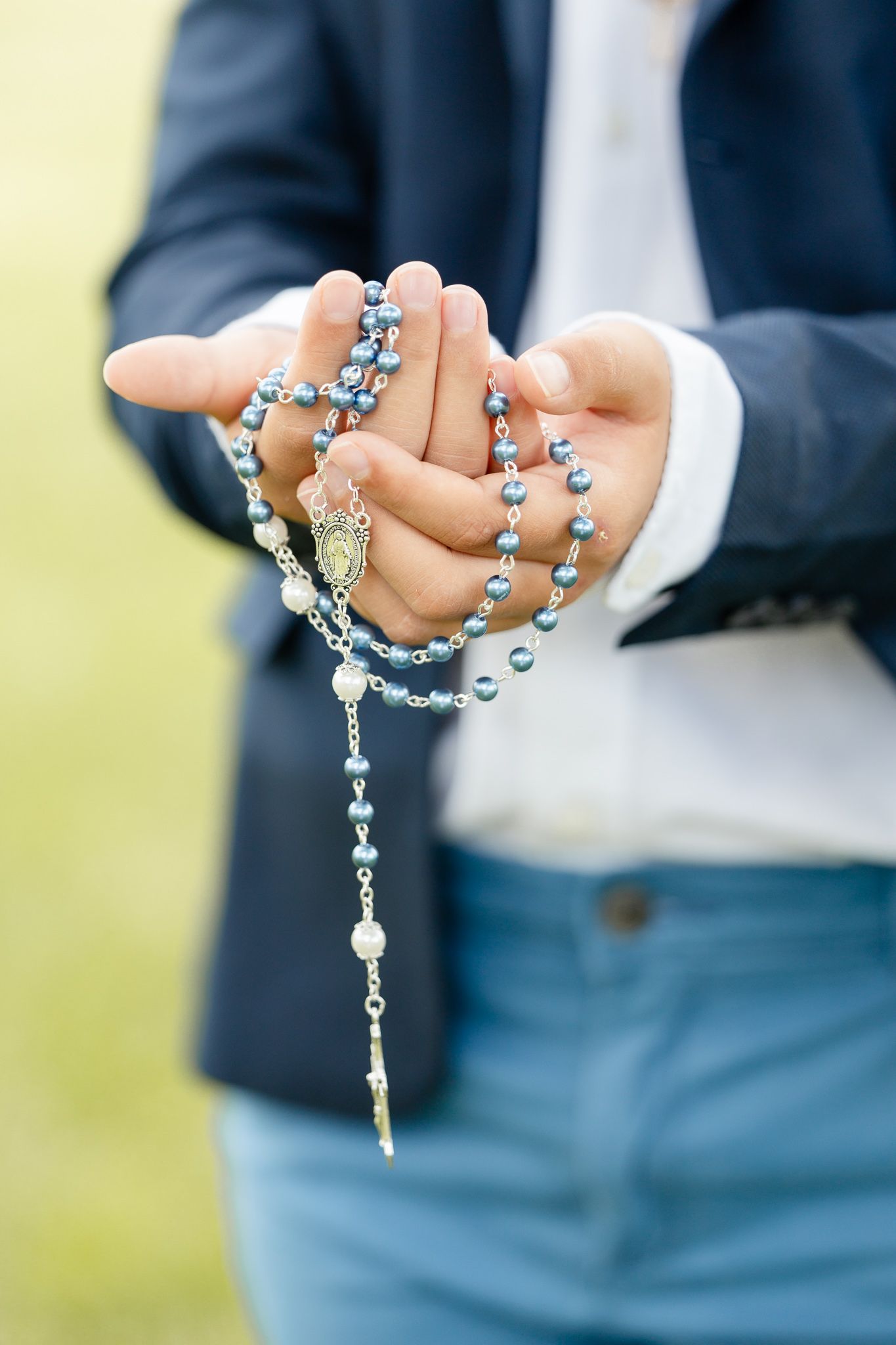 Hands holding an ornate silver rosary with beads against a blurred background.