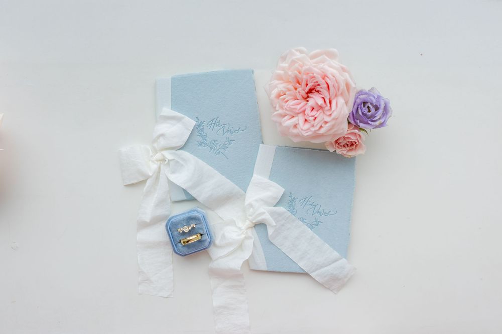 Light blue wedding stationery with white ribbons and pink and purple floral accents.
