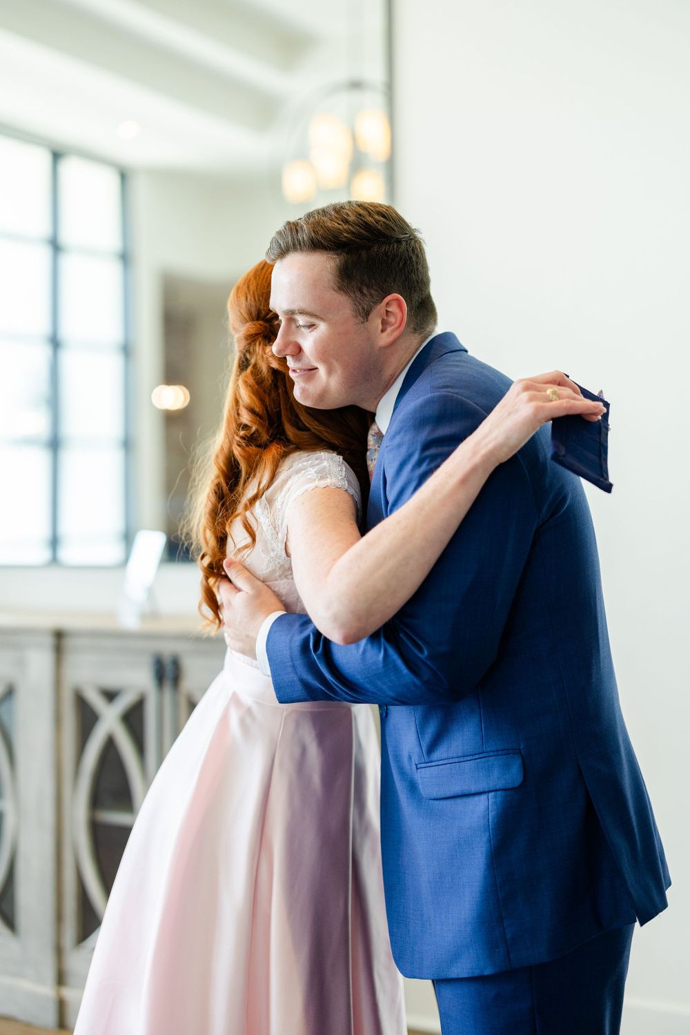 A couple sharing an embrace while wearing formal attire in a bright modern venue.