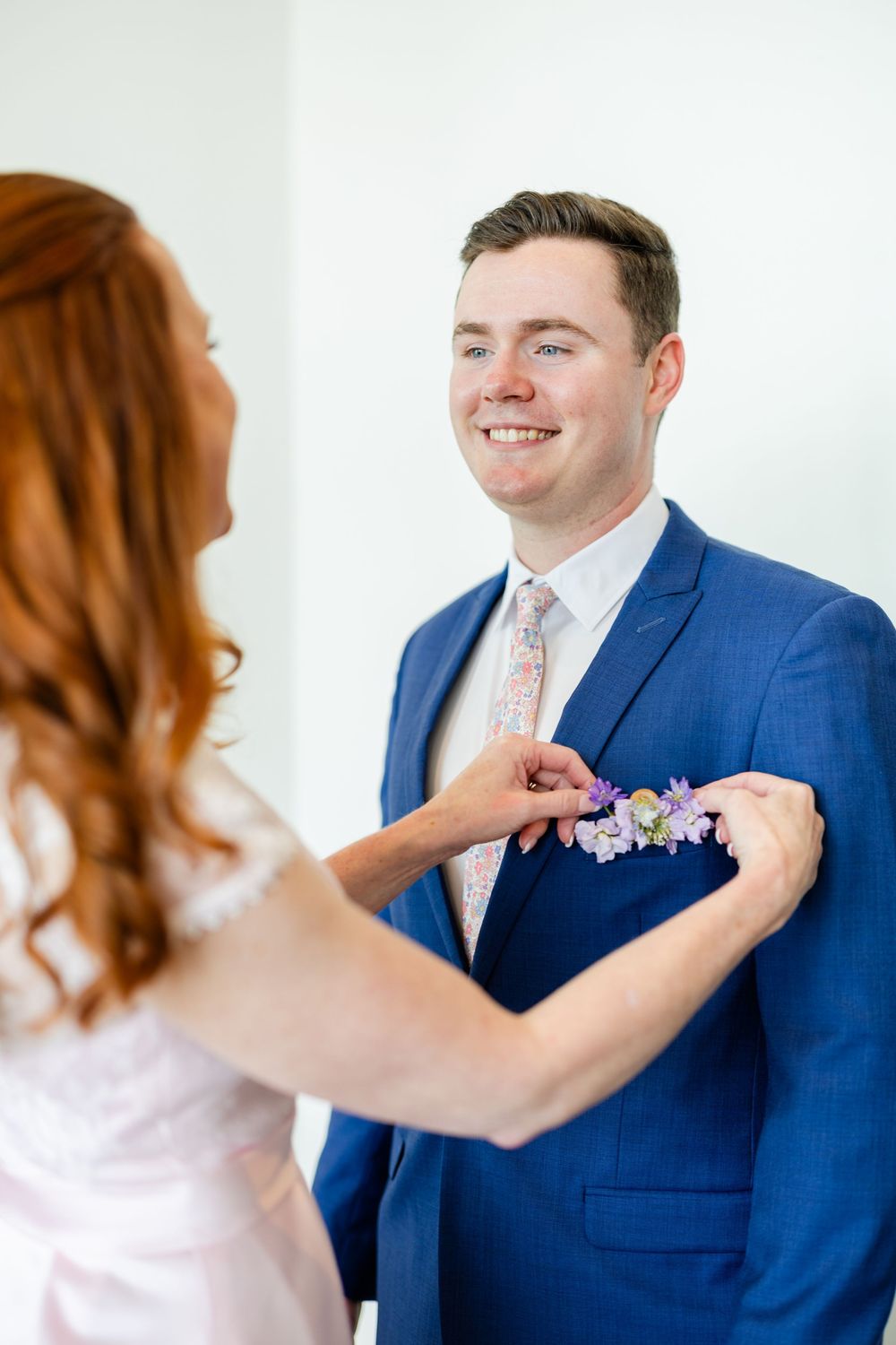 A boutonniere being pinned onto a navy blue suit in an intimate pre-wedding moment.