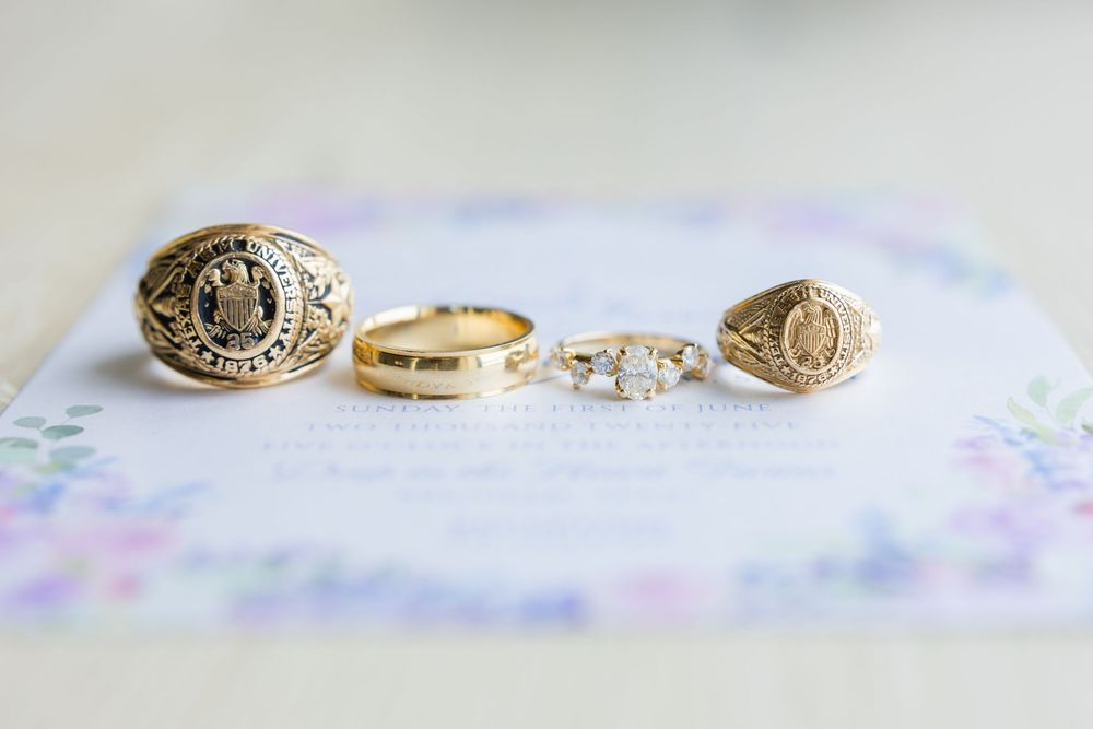 Three vintage gold rings displayed on pastel floral wedding stationery.