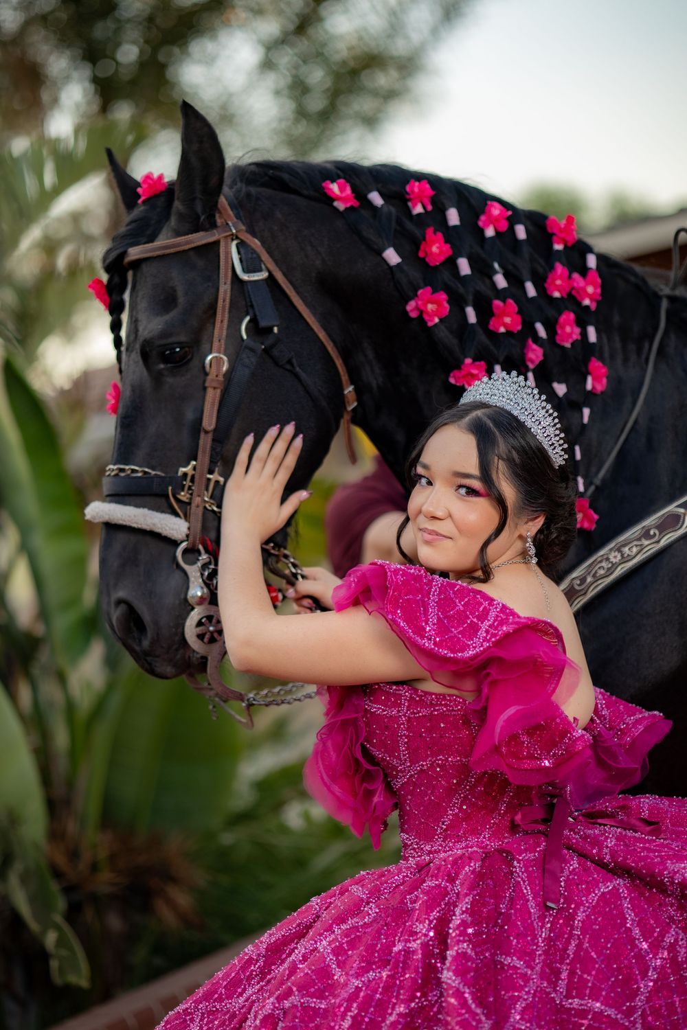 Quinceañera girl in hot pink gown smiles while embracing a flower-decorated black horse.