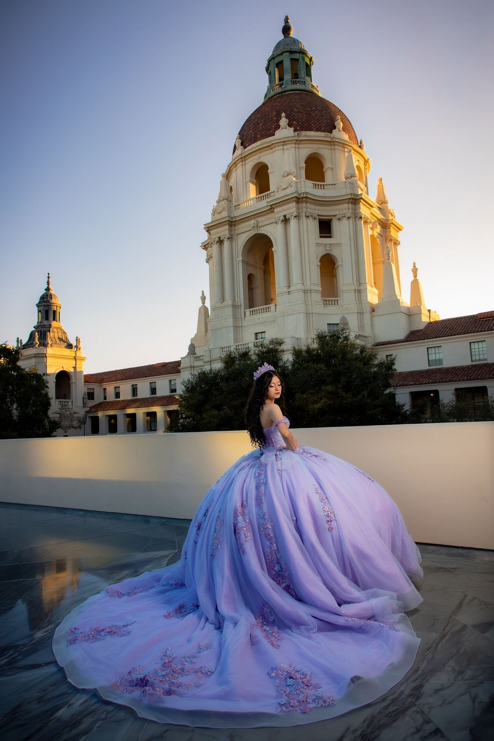 Young woman in lavish purple quinceañera ball gown poses before Pasadena City Hall at sunset.
